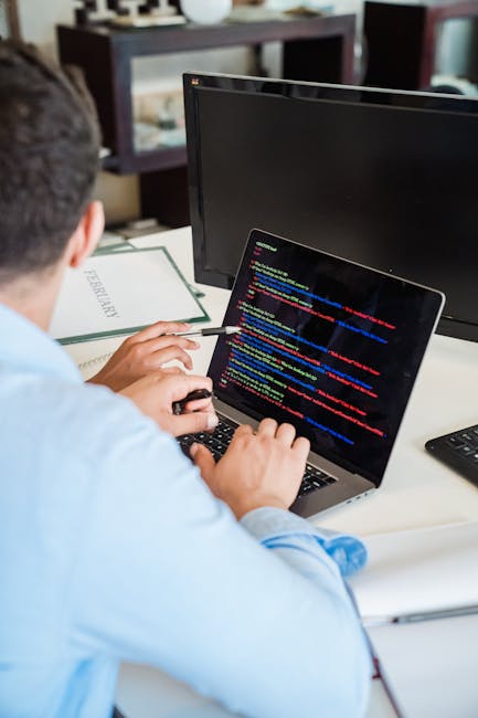A close-up image of a laptop computer displaying lines of code on its screen, with the code written in a dark-themed editor featuring syntax highlighting in bright colors such as green and blue. Next 